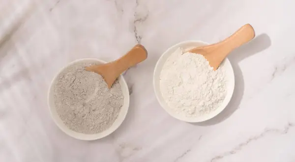 Deux bols de poudre, l'un gris et l'autre blanc, avec des cuillères en bois. L'argile blanche est parfaite pour les cheveux.