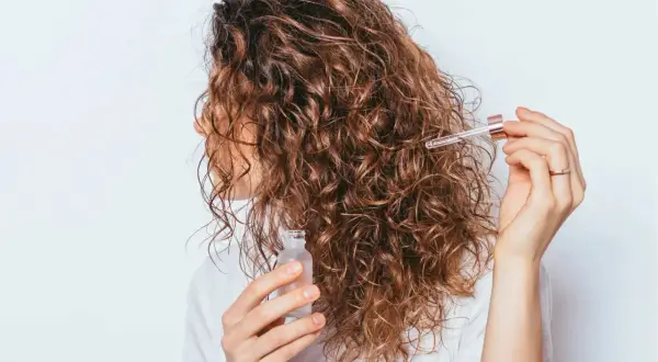 Une femme applique une huile sur ses cheveux bouclés frisottis pour les hydrater.