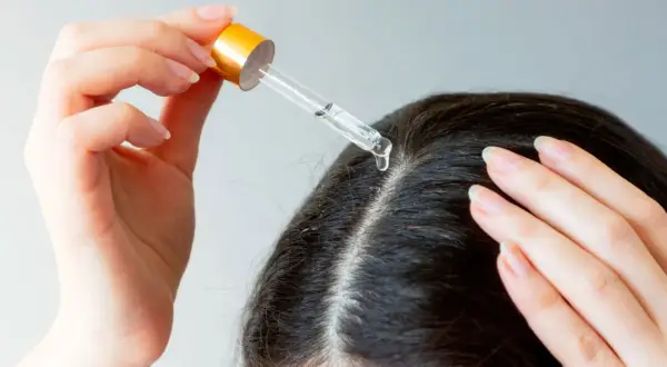 Une main applique une goutte d'huile de chanvre sur le cuir chevelu, une solution naturelle pour les cheveux blancs.