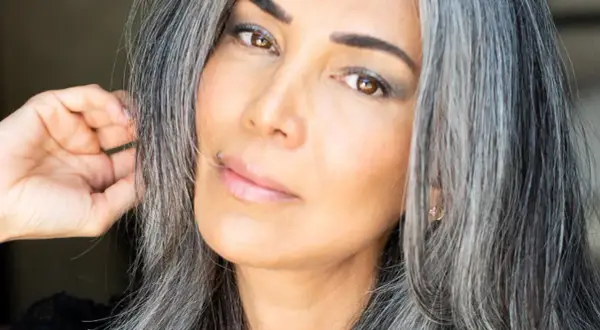 Une femme avec des cheveux gris mi-courts, le regard intense, touche doucement sa chevelure.