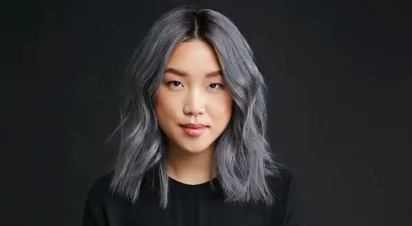 Une jeune femme au teint clair arbore une chevelure mi-longue, ondulée et d'un magnifique gris argenté. Elle porte un haut noir.