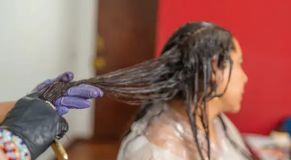 Application d'une patine sur cheveux humides. Une main gantée sépare une mèche pour une application uniforme.