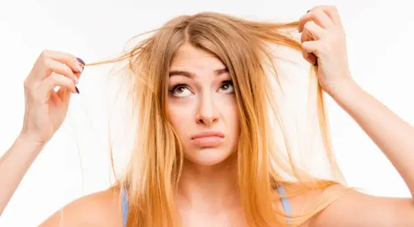 Une jeune femme aux cheveux jaune regarde ses mèches emmêlées avec une expression perplexe.