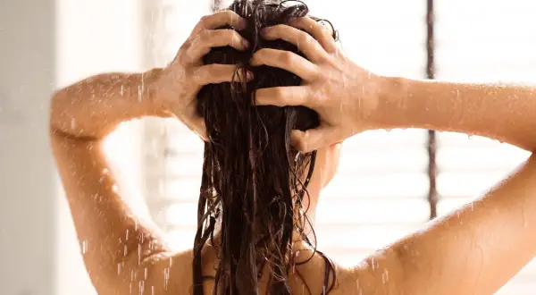 Une personne se lave les cheveux sous la douche, l'eau ruisselant sur son dos et ses bras.