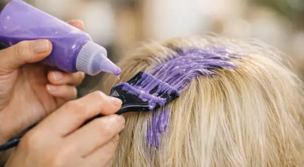 Application d'une patine violette sur des cheveux blonds méchés pour raviver leur éclat.