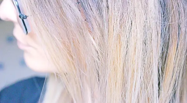 Une femme se regarde dans le miroir, son regard concentré sur l'idée d'enlever une patine cheveux. Ses mèches blondes sont mises en valeur.