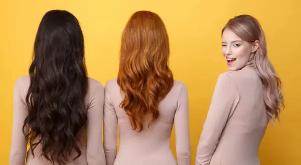 Trois femmes se tiennent côte à côte, montrant la diversité de la couleur cheveux femme : brun foncé, roux flamboyant et blond rosé.