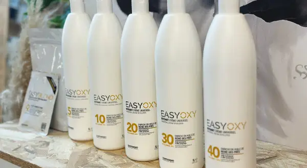 Cinq bouteilles d'oxydant seul pour éclaircir, de différentes forces (5, 10, 20, 30, 40 volumes), sur une étagère en bois.
