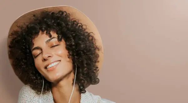 Femme avec une permanente naturelle, un chapeau et des écouteurs, profitant d'un moment de détente.