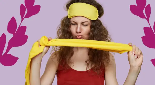 Une femme aux cheveux bouclés, portant un masque de nuit jaune, tient un tissu jaune. Elle semble prête pour une coiffure protectrice nuit.