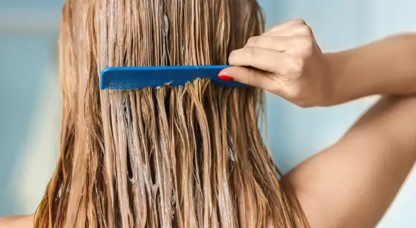 Une main peigne des cheveux blonds mouillés, recouverts d'un soin, peut-être pour changer de couleur de cheveux.