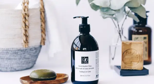 Savon liquide d'Alep pour les cheveux, avec un savon solide et une bouteille pompe. Un panier en osier est visible en arrière-plan.