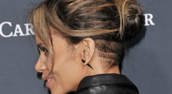 Une femme aux cheveux longs arbore un undercut audacieux avec des motifs rasés sur le côté.
