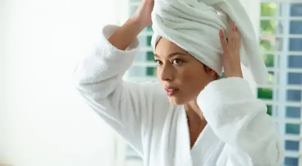 Femme en peignoir blanc, serviette sur la tête, réfléchissant sur le bain d'huile cheveux combien de temps.