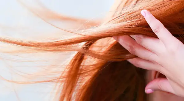 Chevelure rousse flamboyante, une main effleure les mèches. Quelle coloration pour enlever le roux ?