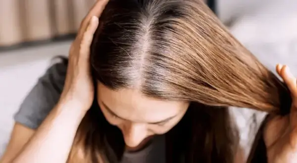 Une femme examine ses racines grasses, cherchant une solution pour sa cure de sebum. Ses mains touchent ses cheveux bruns.
