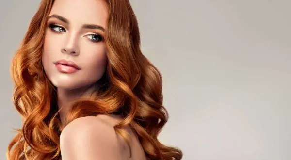 Une femme aux longs cheveux ondulés, d'une magnifique coloration rousse sur brune, pose avec élégance.