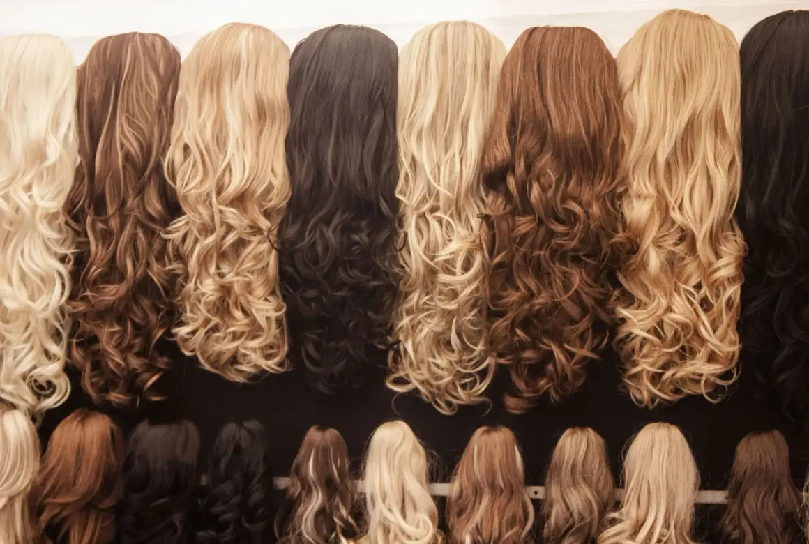 Une rangée de perruques aux ondulations douces, offrant un magnifique mélange couleur cheveux, du blond platine au brun profond.