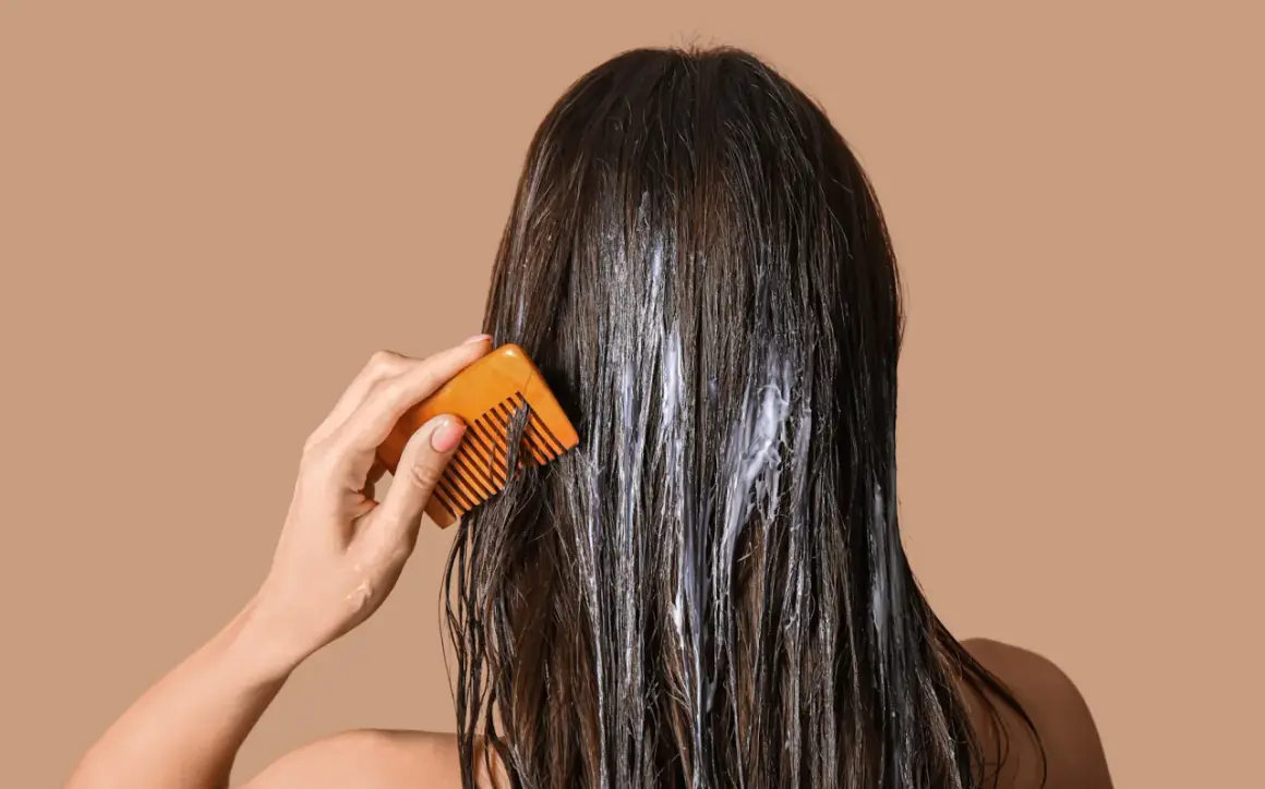 Application d'une coloration végétale sur cheveux. Une main peigne doucement les mèches pour répartir le produit.