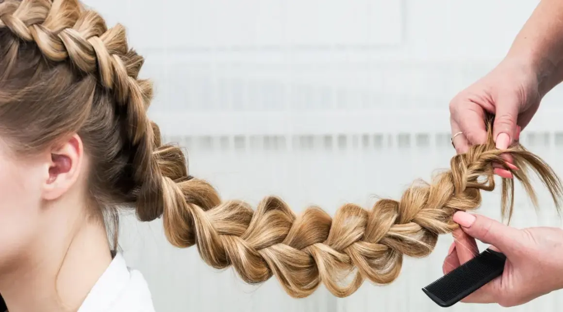 Une main peigne une tresse blonde, une coiffure originale facile à réaliser pour un look sophistiqué.