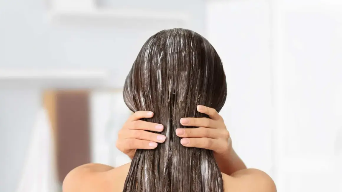 Application d'un soin pour une clarification cheveux. Les mains appliquent le produit sur les longueurs.