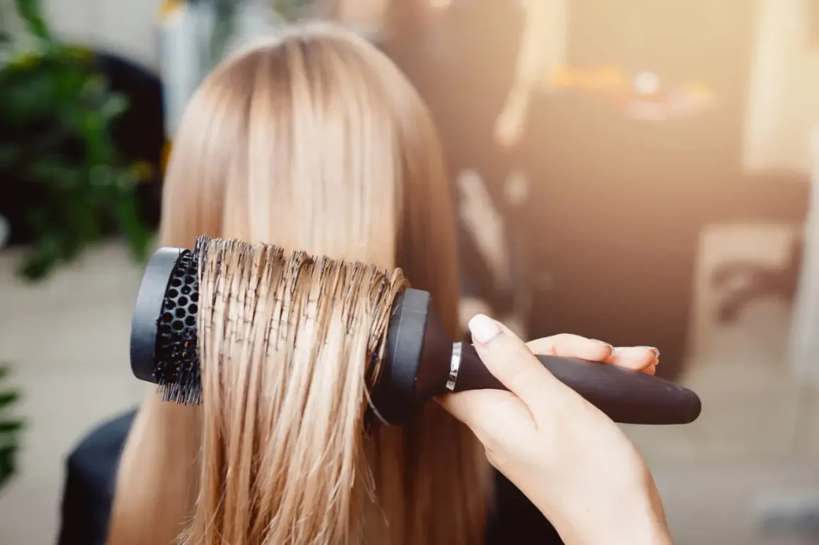 Main d'un coiffeur effectuant un brushing sur des cheveux blonds.