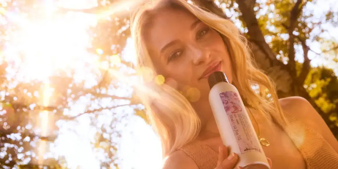 Une femme aux cheveux blonds, avec un balayage naturel, tient un produit Davines sous un soleil éclatant.