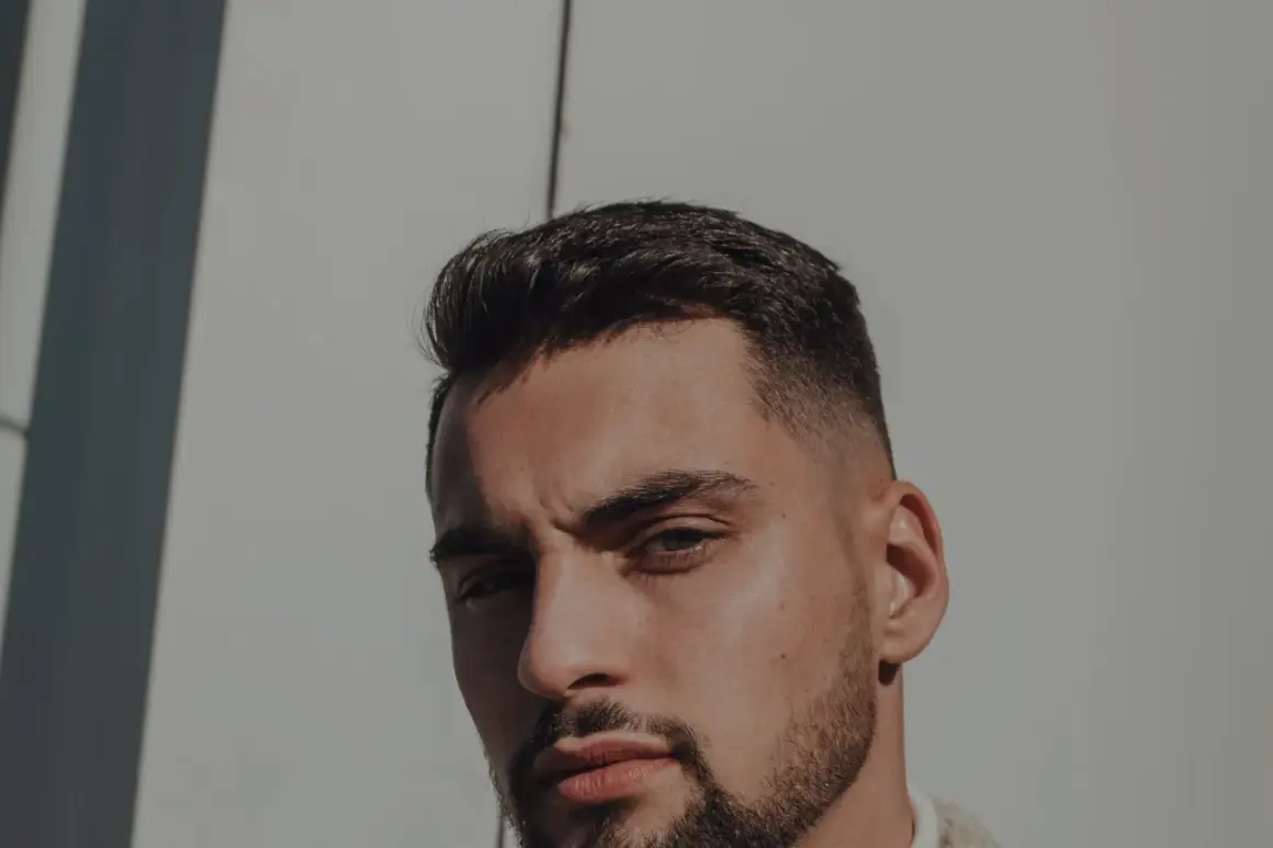 Un homme au chignon homme rasé, regard intense, sous un soleil éclatant.