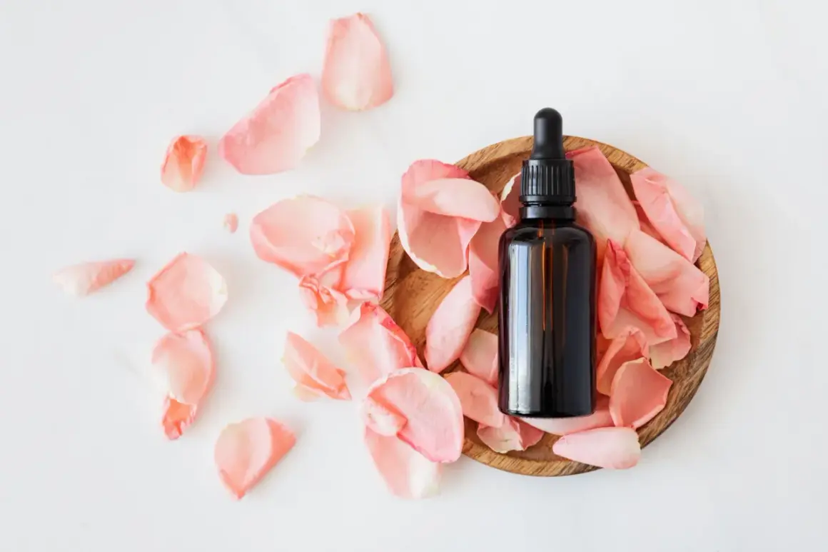 Flacon d'huile essentielle sur un lit de pétales de rose, idéal pour les cheveux gras.