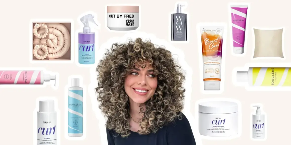 Une femme aux cheveux bouclés souriante, entourée de produits pour une routine cheveux bouclés : sprays, masques, gels et conditionneurs.