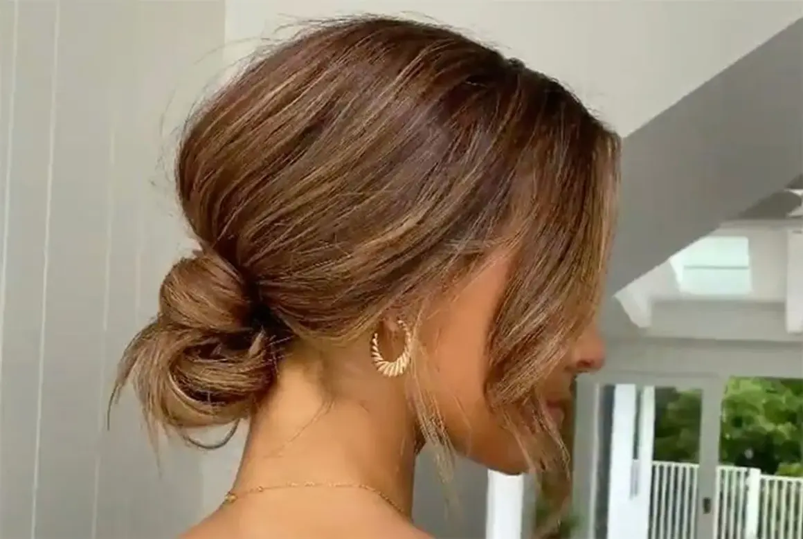 Une coiffure élégante avec un chignon bouclé flou, des mèches encadrant le visage et des boucles d'oreilles dorées.