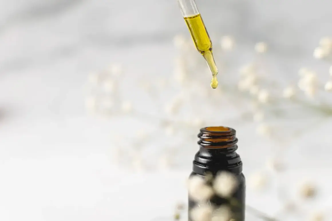 Goutte d'huile de jojoba tombant d'une pipette sur un flacon ambré. Idéal pour des cheveux transformés, avant après.