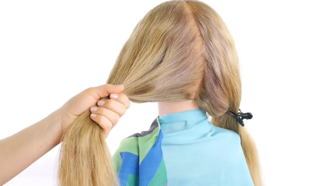 Main d'une femme tenant une mèche de cheveux blonds pour commencer une tresse hollandaise.