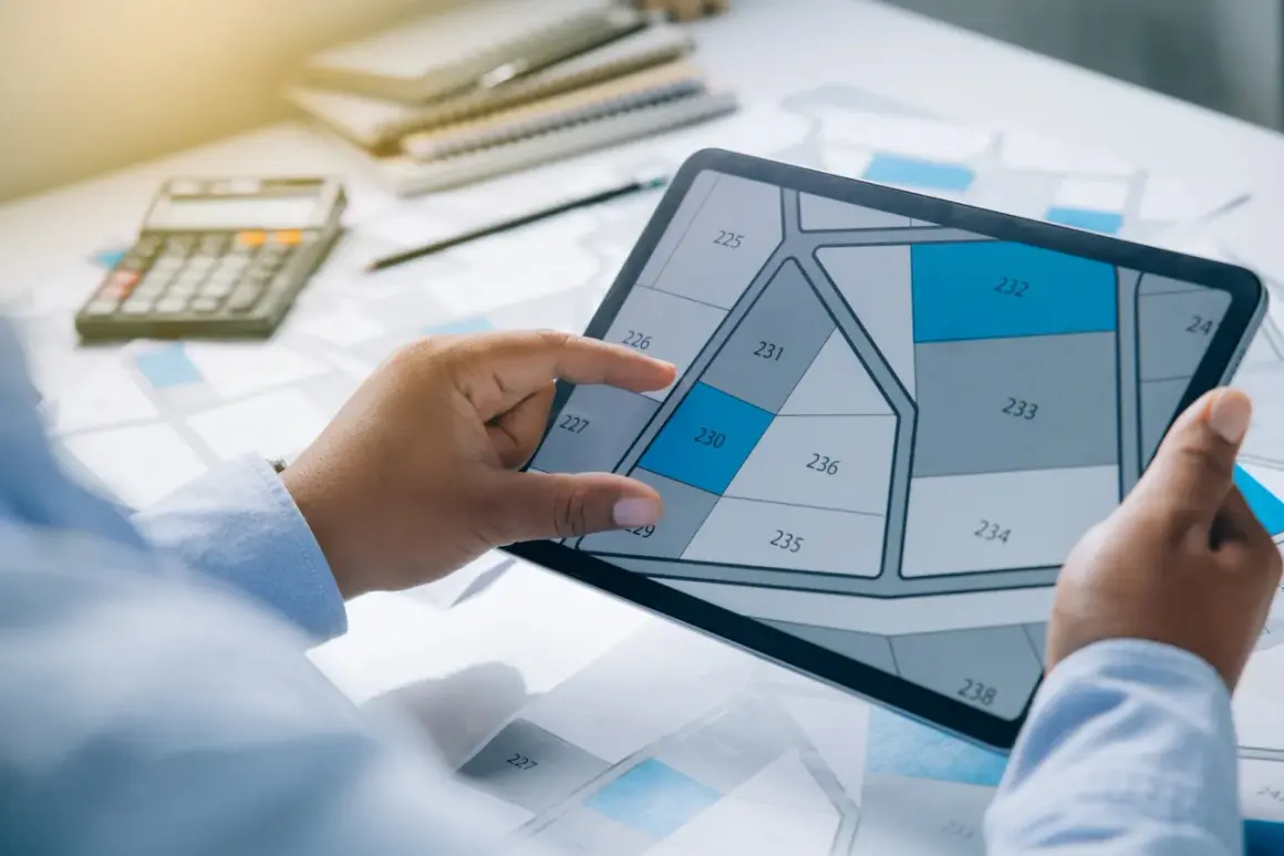 Une personne examine un plan de parcelle sur une tablette, calculant peut-être combien coûte une permanente pour un projet.