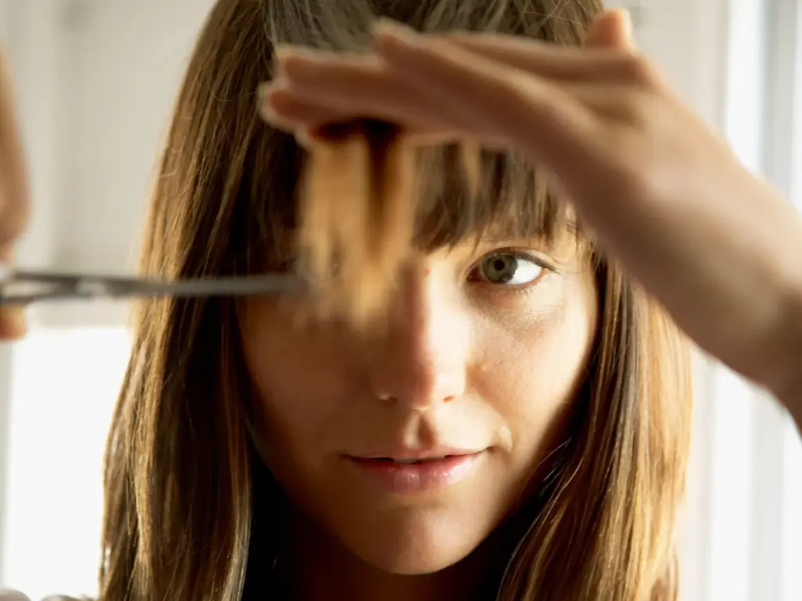 Une femme se coupe les pointes des cheveux. Elle hésite sur combien de cm couper.