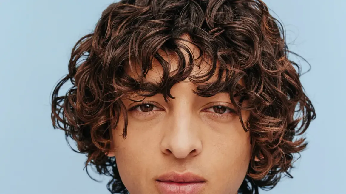Gros plan sur un visage aux yeux marron et à la coiffure cheveux frisés bruns et volumineux.
