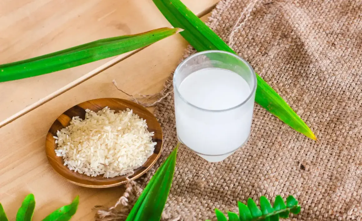 Un bol de riz cru et un verre d'eau de riz, parfaits pour des cheveux brillants.
