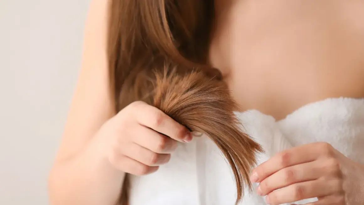Une femme examine ses cheveux, cherchant des conseils pour comment éviter les fourches et garder une chevelure saine.