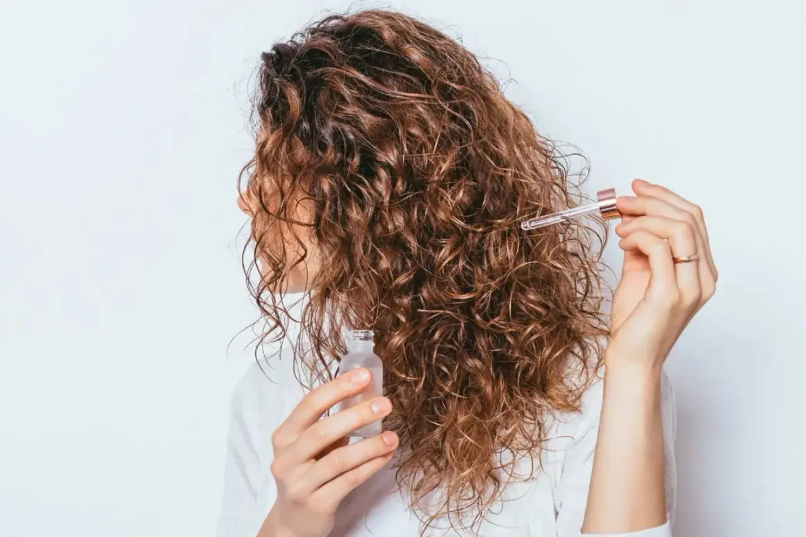 Une femme applique une huile sur ses cheveux bouclés frisottis pour les hydrater.
