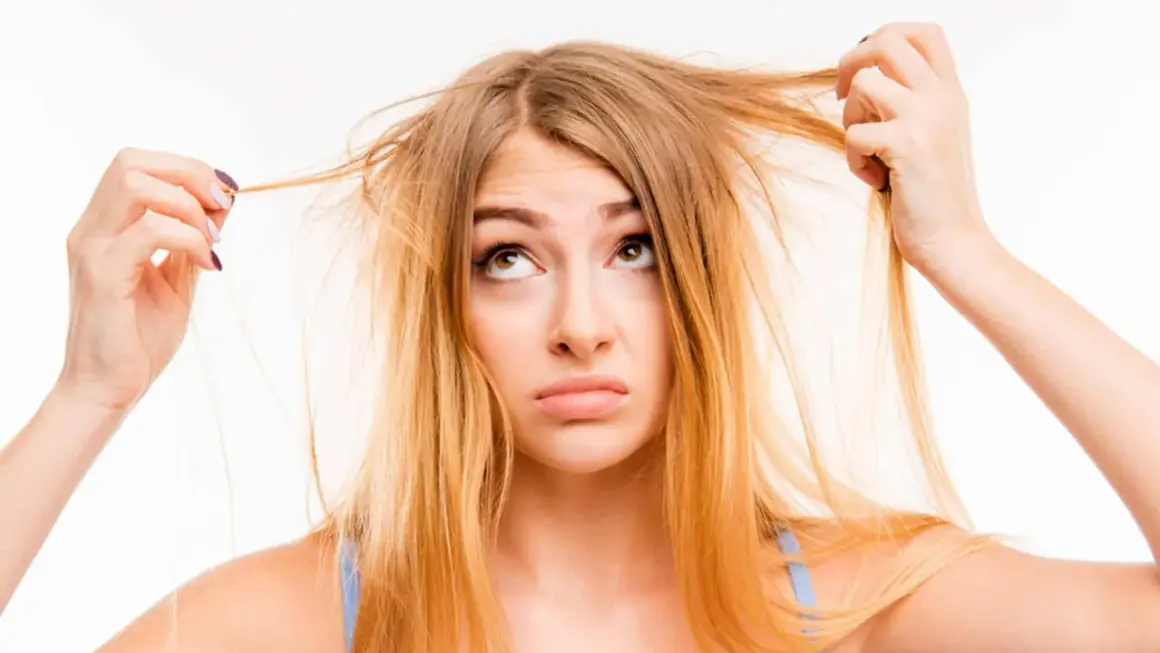 Une jeune femme aux cheveux jaune regarde ses mèches emmêlées avec une expression perplexe.