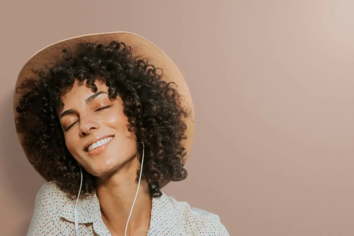Femme avec une permanente naturelle, un chapeau et des écouteurs, profitant d'un moment de détente.