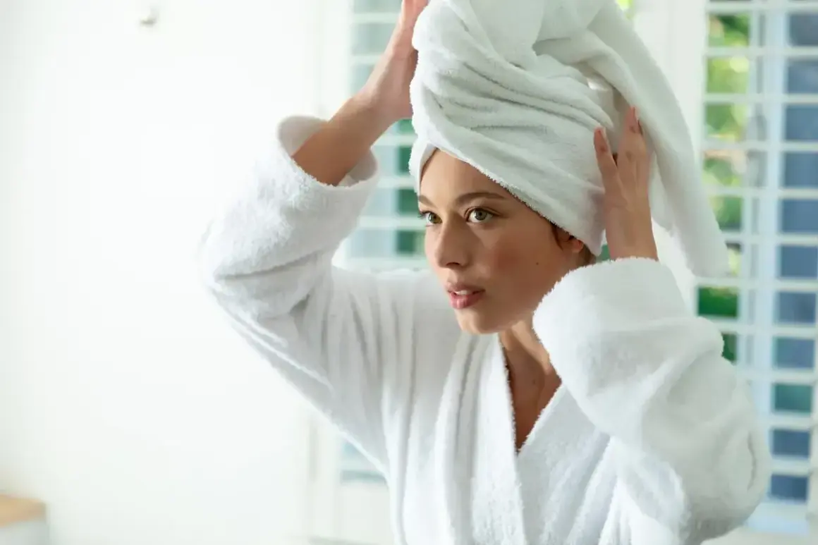 Femme en peignoir blanc, serviette sur la tête, réfléchissant sur le bain d'huile cheveux combien de temps.