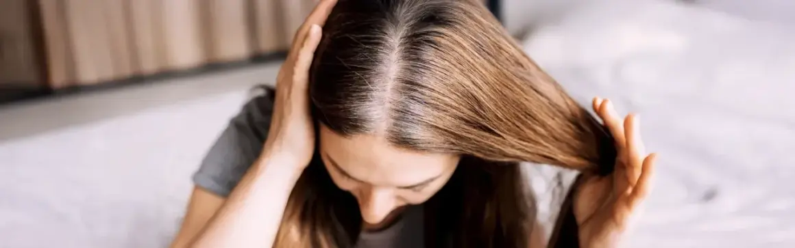 Une femme examine ses racines grasses, cherchant une solution pour sa cure de sebum. Ses mains touchent ses cheveux bruns.