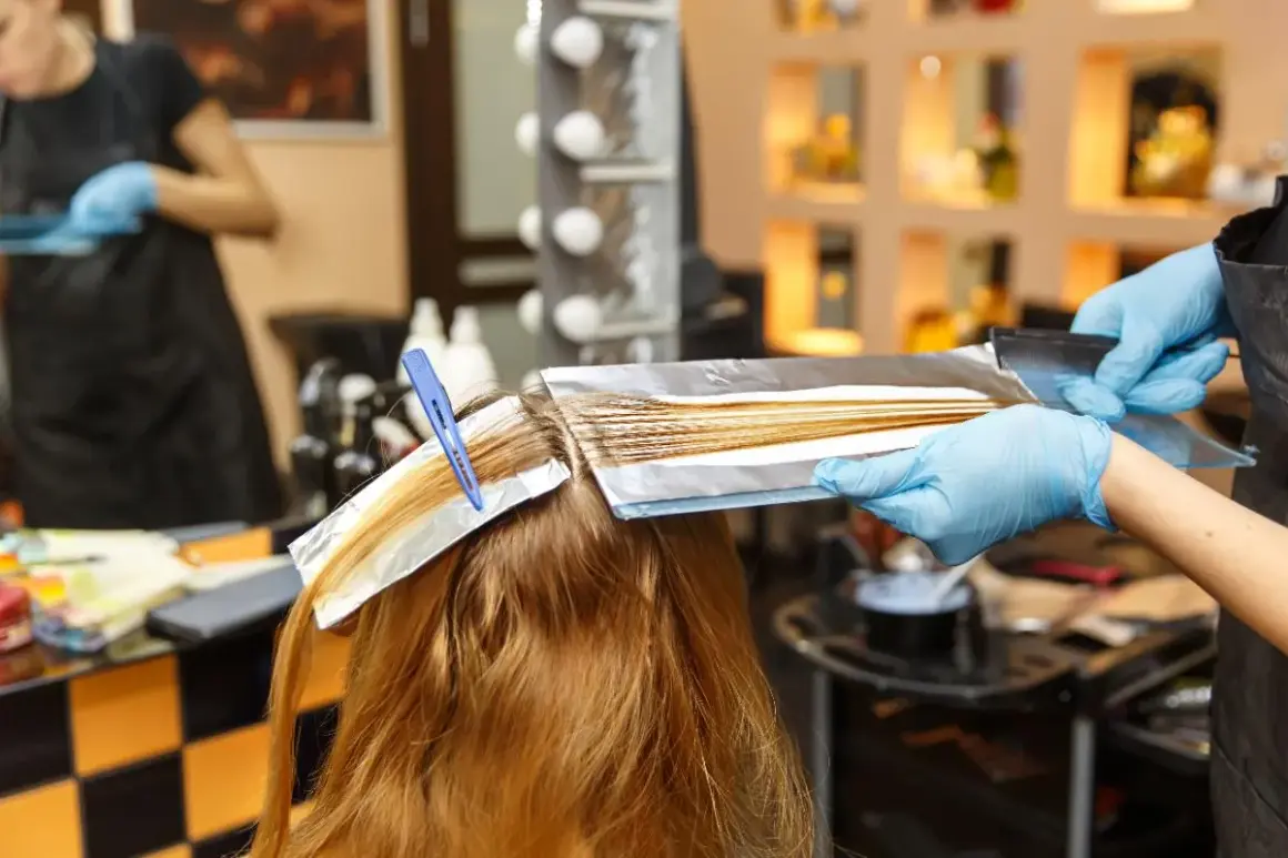 Coiffure : une main gantée applique une décoloration sur des mèches fines, une technique pour comment faire ses racines quand on a des mèches.