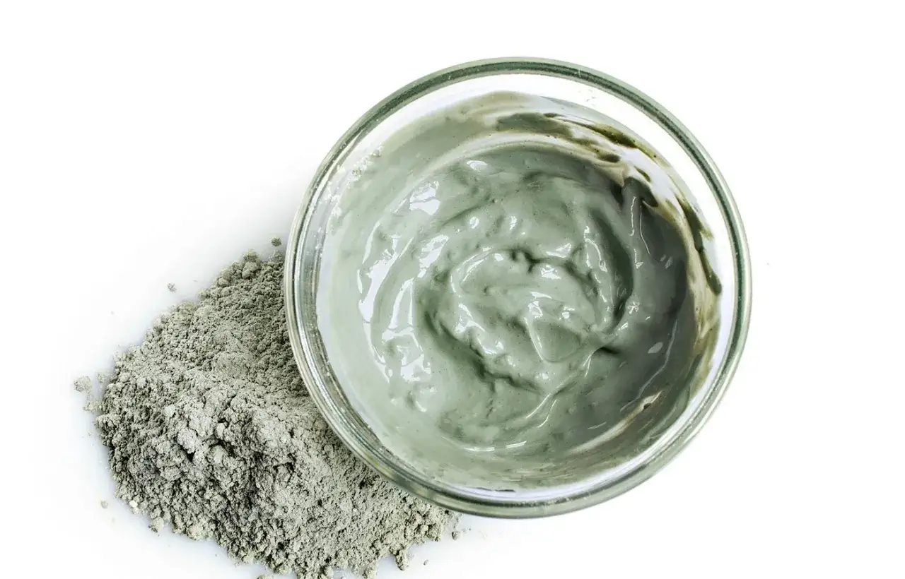 Un bol de masque à l'argile verte, prêt à être appliqué sur des cheveux colorés pour un soin revitalisant.