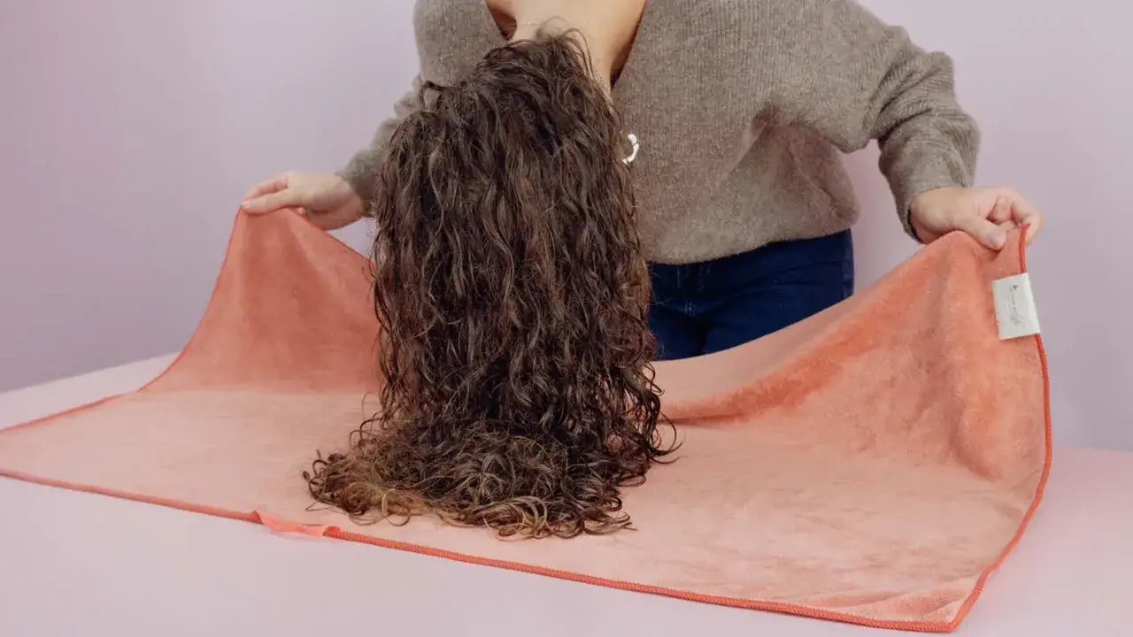 Une personne incline la t&ecirc;te, laissant tomber ses cheveux essor&eacute;s sur une serviette corail.