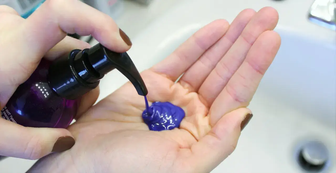 Une main pompe du shampoing bleu dans une autre main. Astuce pour savoir comment enlever le shampoing bleu sur les cheveux.