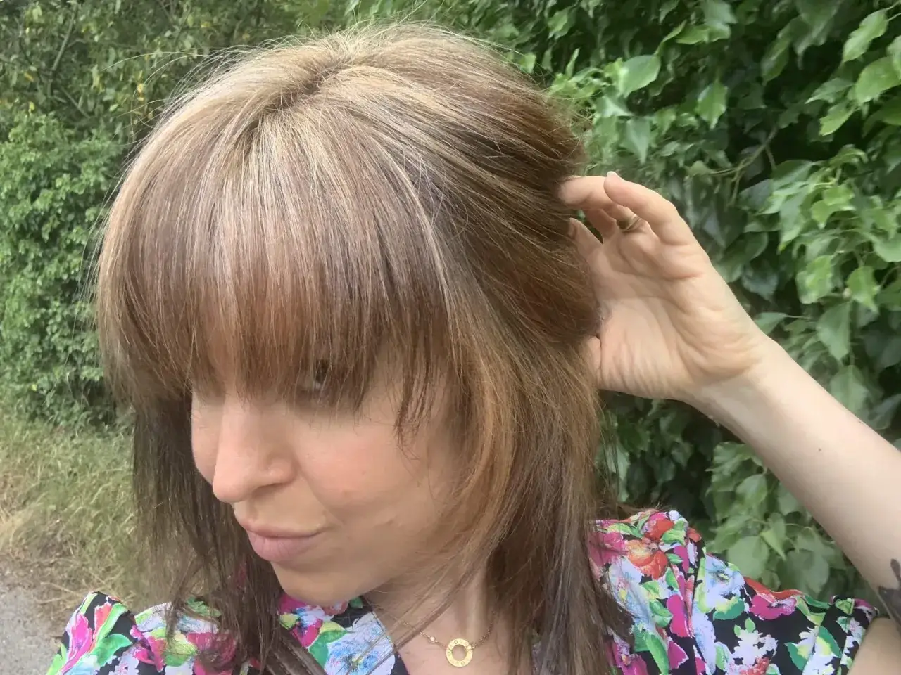 Une femme aux cheveux châtains avec des reflets blonds, touchant sa chevelure. Elle semble vouloir éclaircir ses cheveux naturellement.