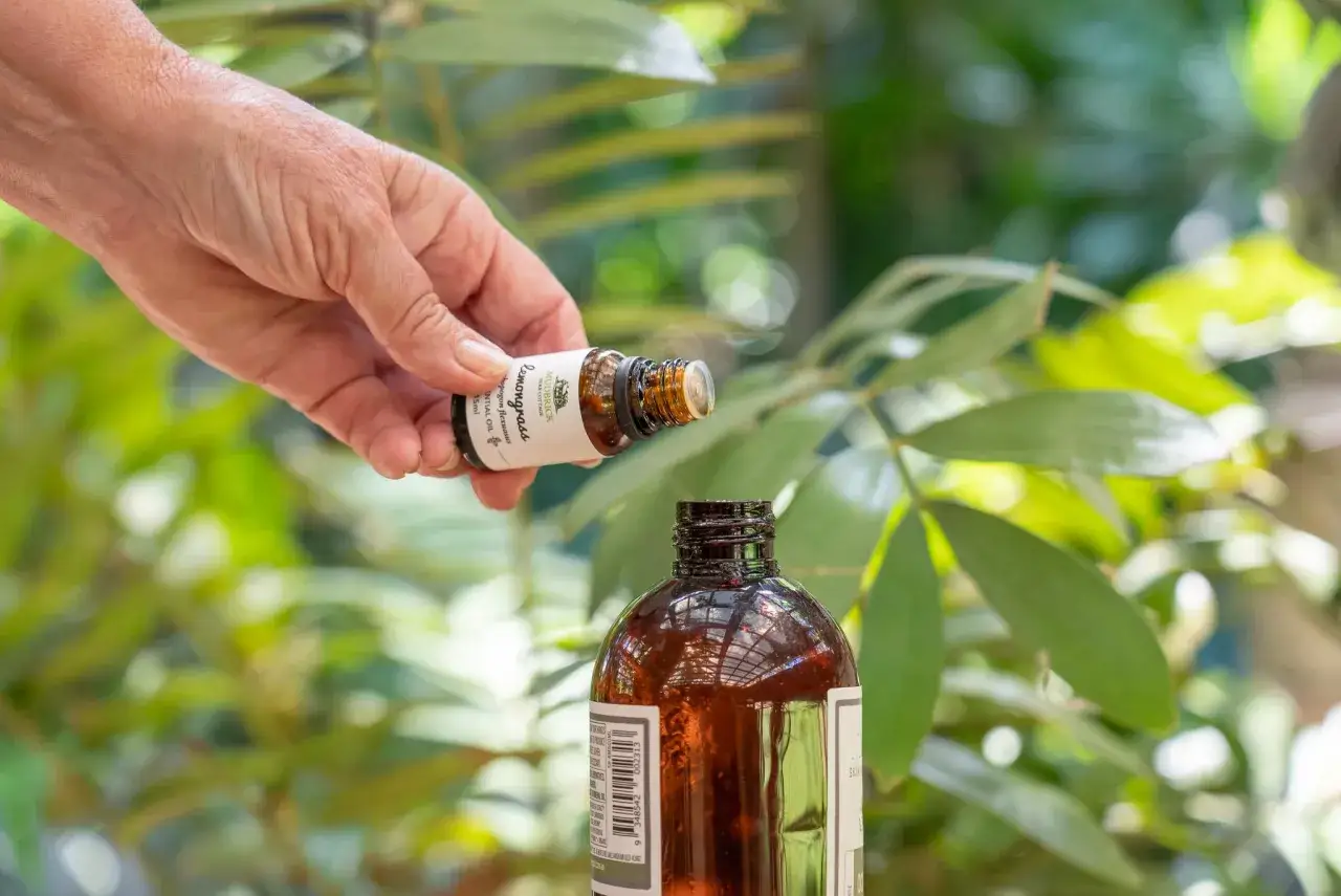 Une main verse une goutte d'huile essentielle de citronnelle dans une bouteille, un geste pour favoriser la pousse des cheveux.