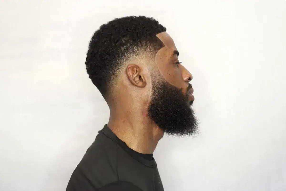 Profil d'un homme avec une barbe soign&eacute;e et une coupe de cheveux d&eacute;grad&eacute;e, mettant en valeur un taper fase impeccable.
